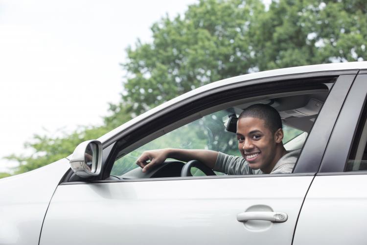 Young male leaning out the window of his car smiling for the camera. 